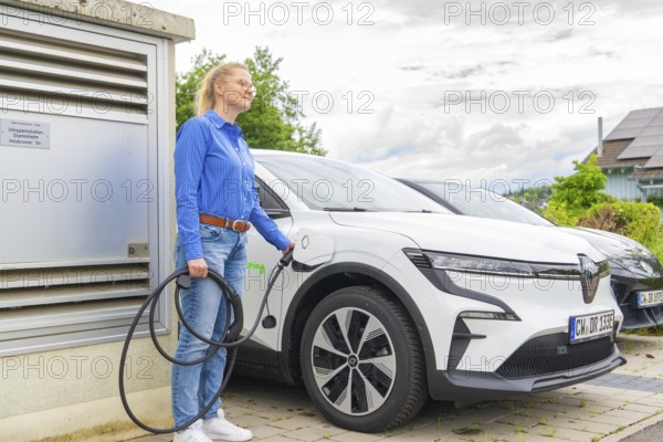 Woman wearing a blue shirt charges a white electric car at a charging station, Deer E-Carsharing,