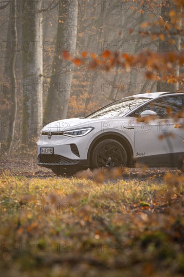 A white car drives on a forest path surrounded by autumn trees, Deer E-Carsharing, VW ID4, Calw,