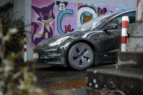 Black car in an urban environment with colorful graffiti wall and wet road, Deer e-Carsharing,