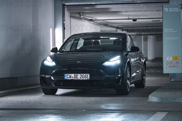Black car drives into a modern, well-lit garage with cool atmosphere, Deer E-Carsharing, Tesla