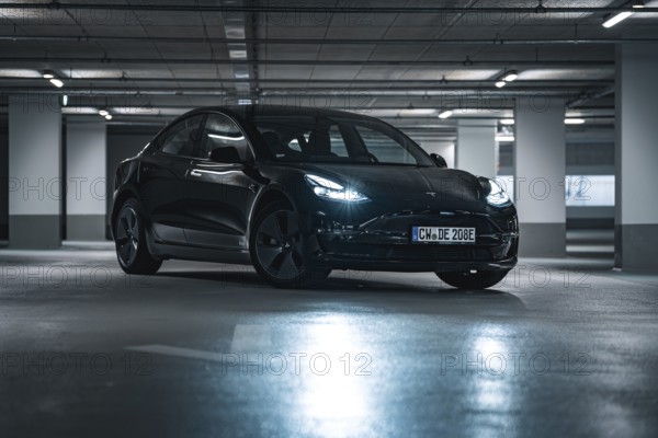 Black car parked in an urban underground car park surrounded by cool artificial light and shade,