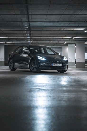 Black car in a modernly lit parking garage at night with reflective floor surfaces, Deer e-car