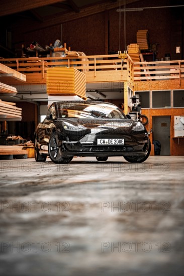 Black car in an industrial-looking workshop with wooden details, parked on concrete floor, deer