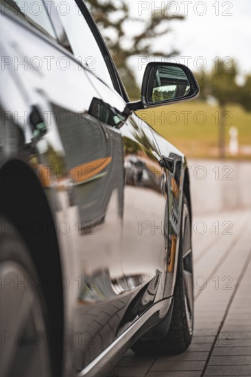 Side view of a reflecting black car, in focus a side mirror, Deer E-Carsharing, Tesla Model 3,