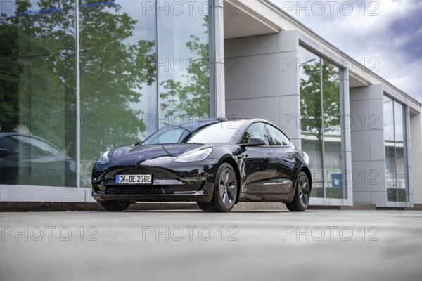 Black Tesla in front of a glass building with trees in the background, Deer e-Carsharing, Tesla