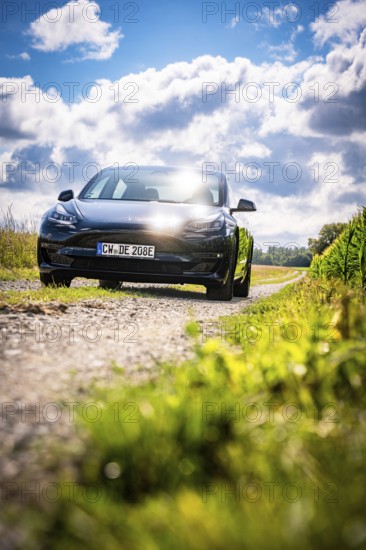 Black car driving on a dirt road through picturesque landscape under blue sky, Deer E-Carsharing,