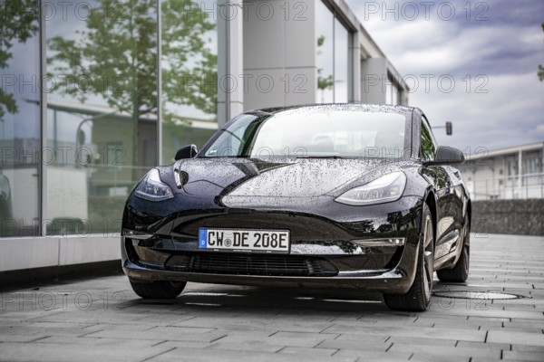Wet Tesla in front of a modern glass building, covered with raindrops, Deer E-Carsharing, Tesla