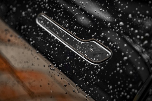 Close-up of a black car with water droplets on the surface showing shiny details, Deer E- car