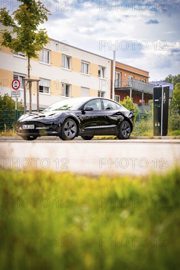 Black car at a charging station in front of a modern building backdrop under a blue sky, Deer