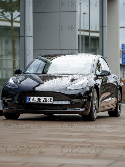 Black car with rain droplets on paint in front of glass buildings, Deer E-Carsharing, Tesla Model