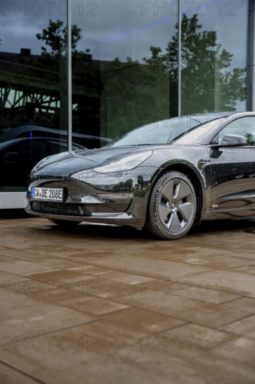 Black car in front of a glass building on rain-wet ground, Deer E-Carsharing, Tesla Model 3, Calw,