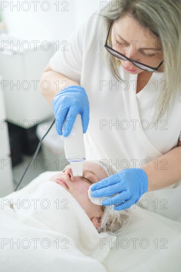 A pro esthetician cosmetologist uses a metal spatula for ultrasonic facial cleansing to exfoliate