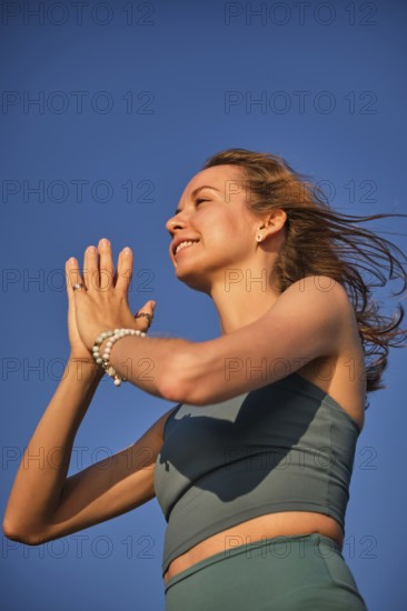 A woman practices yoga on the beach during sunset, holding her hands in Namaskar Mudra while
