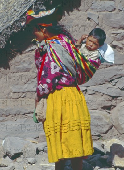 Young woman wearing traditional clothing carries her small child in a traditional way on Isla
