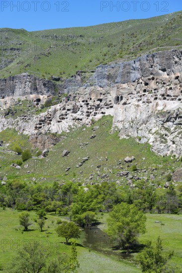 Rocks with engraved caves surrounded by green grass and trees, cave town, cave monastery, Kura