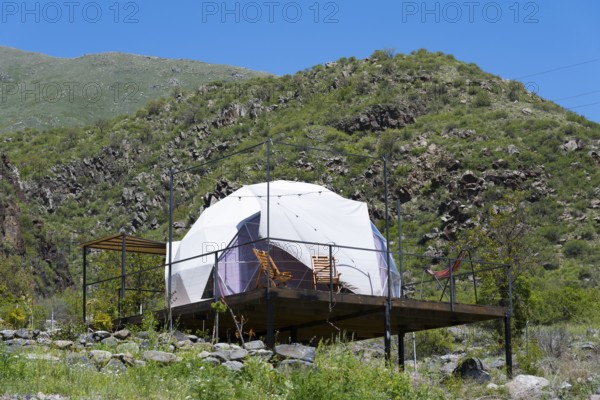 Dome tent on a wooden terrace in green mountain landscape under blue sky, Vardzia Glamping,