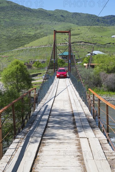 A car drives across a wooden suspension bridge in green surroundings, Kura River near Nijgori,