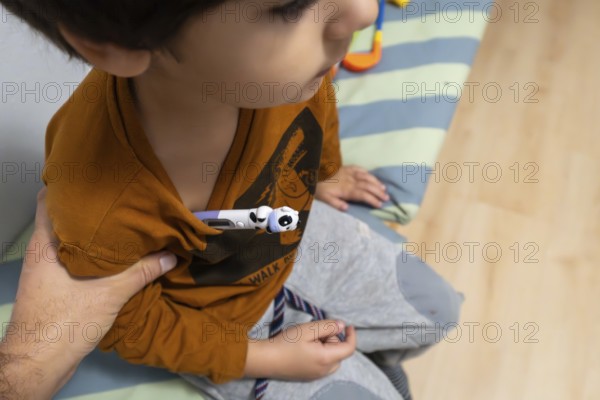 Child wearing a t shirt having a digital thermometer placed under arm for temperature measurement,