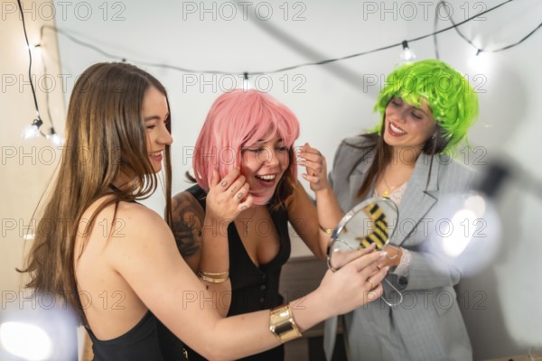 Group of happy young women friends trying on fun colorful wigs and preparing for a costume party or