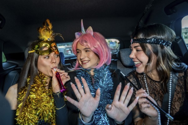 Three young women in festive costumes ride in a car, wearing tinsel and makeup, laughing and