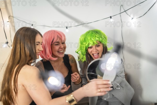 Two young women in pink and green wigs laugh and celebrate at a colorful house party, sharing