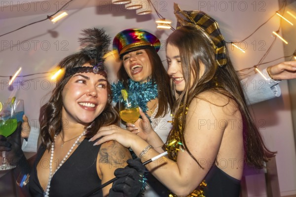 Young women in festive costumes laugh and toast cocktails at a colorful new year's eve home party,
