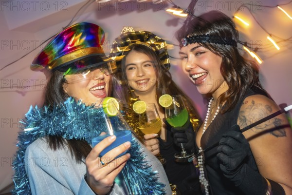 Three happy young women laughing and drinking colorful cocktails while celebrating a new year's eve