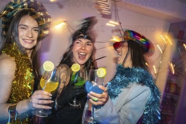 Diverse women in festive party hats and tinsel clink colorful lime garnished cocktails, laughing