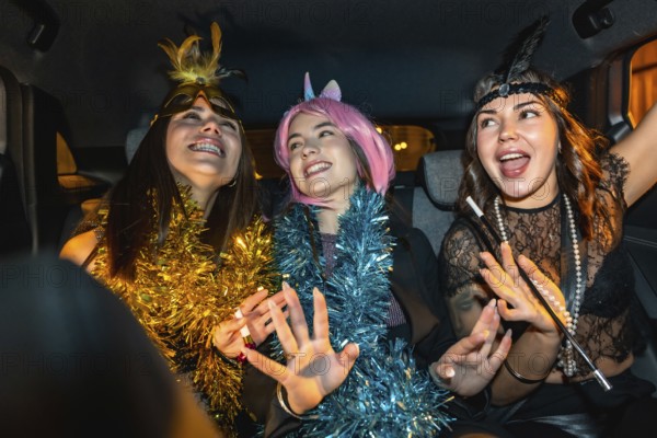 Three happy young women celebrating and having fun during a night car ride, dressed in festive