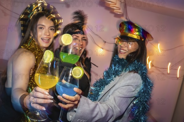 Three happy young women celebrating a party, toasting colorful cocktails with lime slices, laughing