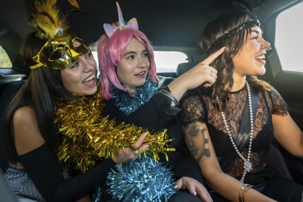 Three young women dressed in cheerful costumes with tinsel on the back seats of a car, joyfully