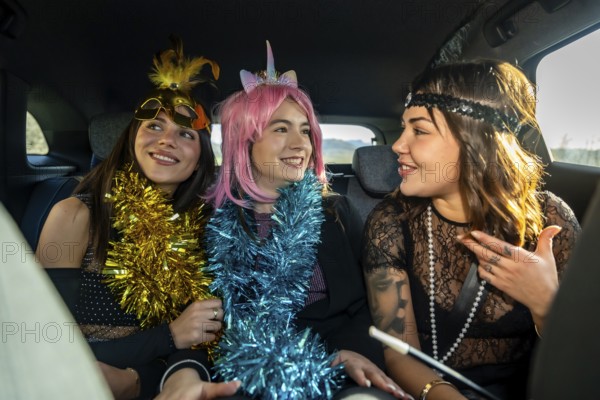 Three young women in colorful costume accessories and party attire laughing and talking in the back