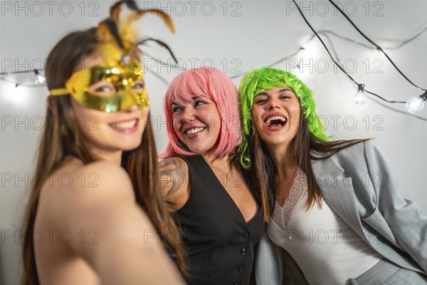 Three young adult female friends laughing and enjoying a costume party with vibrant wigs and golden