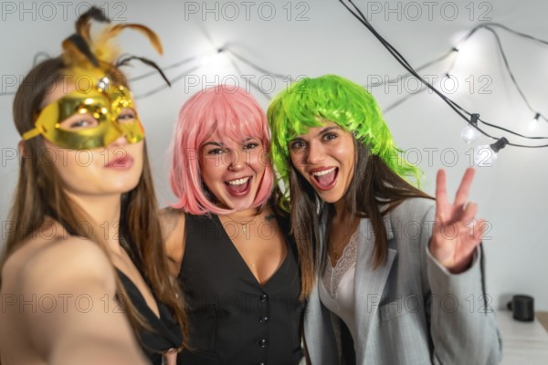 Three young women in colorful wigs and a masquerade mask laugh and pose for a bright, carefree