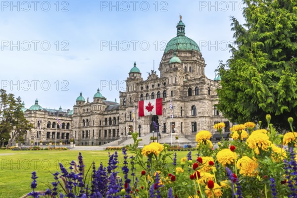 The british columbia parliament buildings are shown displaying a large canadian flag during summer