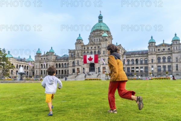 Mother and son running on the lawn in front of the british columbia parliament buildings in