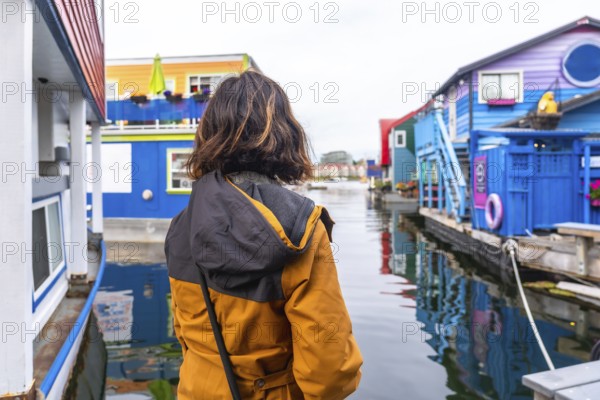 Tourist wearing a yellow jacket is enjoying the view of the colorful floating houses in fisherman's