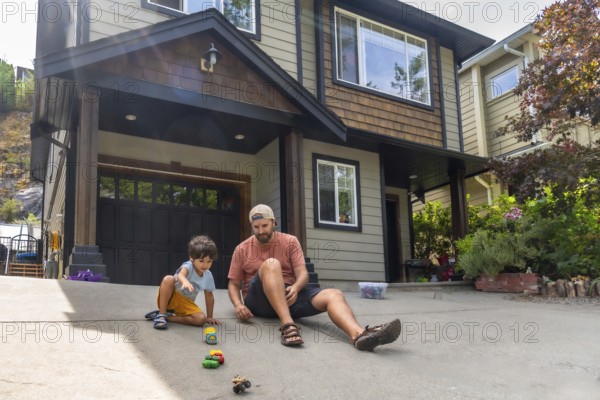 Father and son are sitting on their driveway, playing with a collection of toy cars in front of