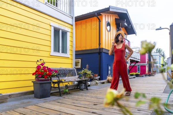 Tourist wearing jumpsuit and straw hat walking on wooden walkway in front of colorful floating