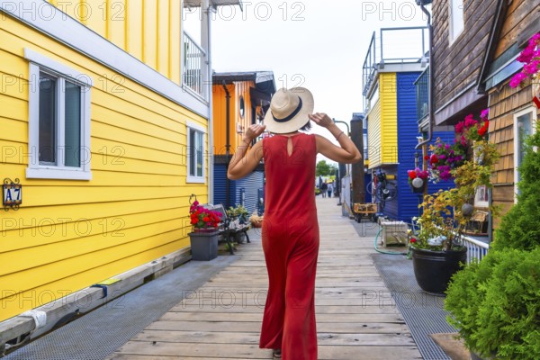 Tourist wearing a straw hat and red dress walking along the wooden boardwalk at fisherman's wharf