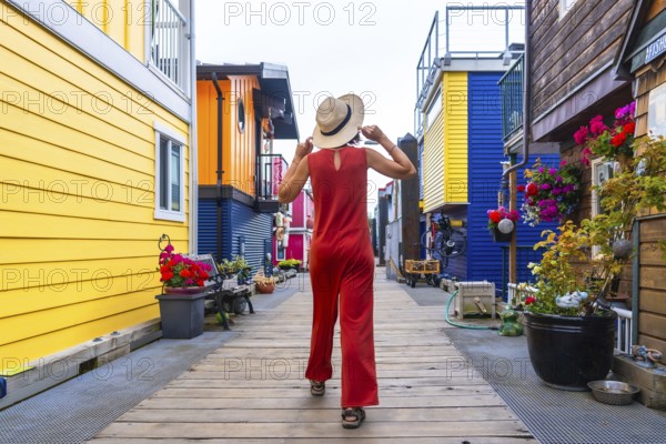 Tourist wearing a straw hat and red jumpsuit walking along a wooden walkway by vibrant floating