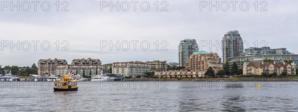 Yellow water taxi sailing in victoria, british columbia inner harbor with cityscape, condominiums,