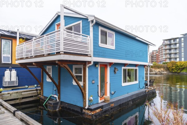 Colorful floating home with a white balcony and orange door reflecting in calm waters of victoria