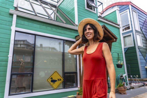 Happy tourist adjusting her straw hat while walking and smiling in front of colorful floating