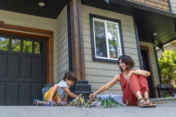 Mother and son sitting on the pavement in front of their house, joyfully playing with colorful