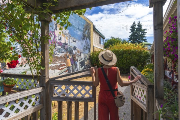 Female tourist in a straw hat and red jumpsuit opening a wooden gate to admire a vibrant mural