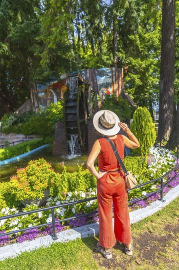 Female tourist wearing a straw hat and a jumpsuit is admiring a watermill and a colorful mural in a