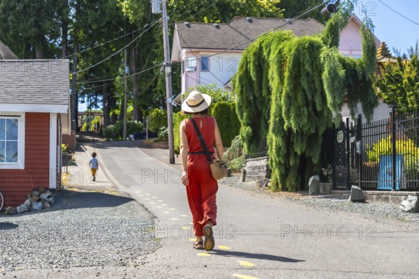 Tourist wearing a straw hat and orange jumpsuit walking along a yellow dotted line on a sunny