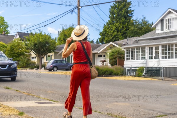 Tourist wearing a straw hat and red jumpsuit walking along a sunny sidewalk in chemainus, vancouver