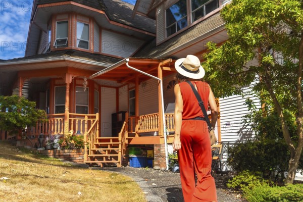 Tourist wearing a straw hat and a red jumpsuit is walking on a path near a traditional wooden house